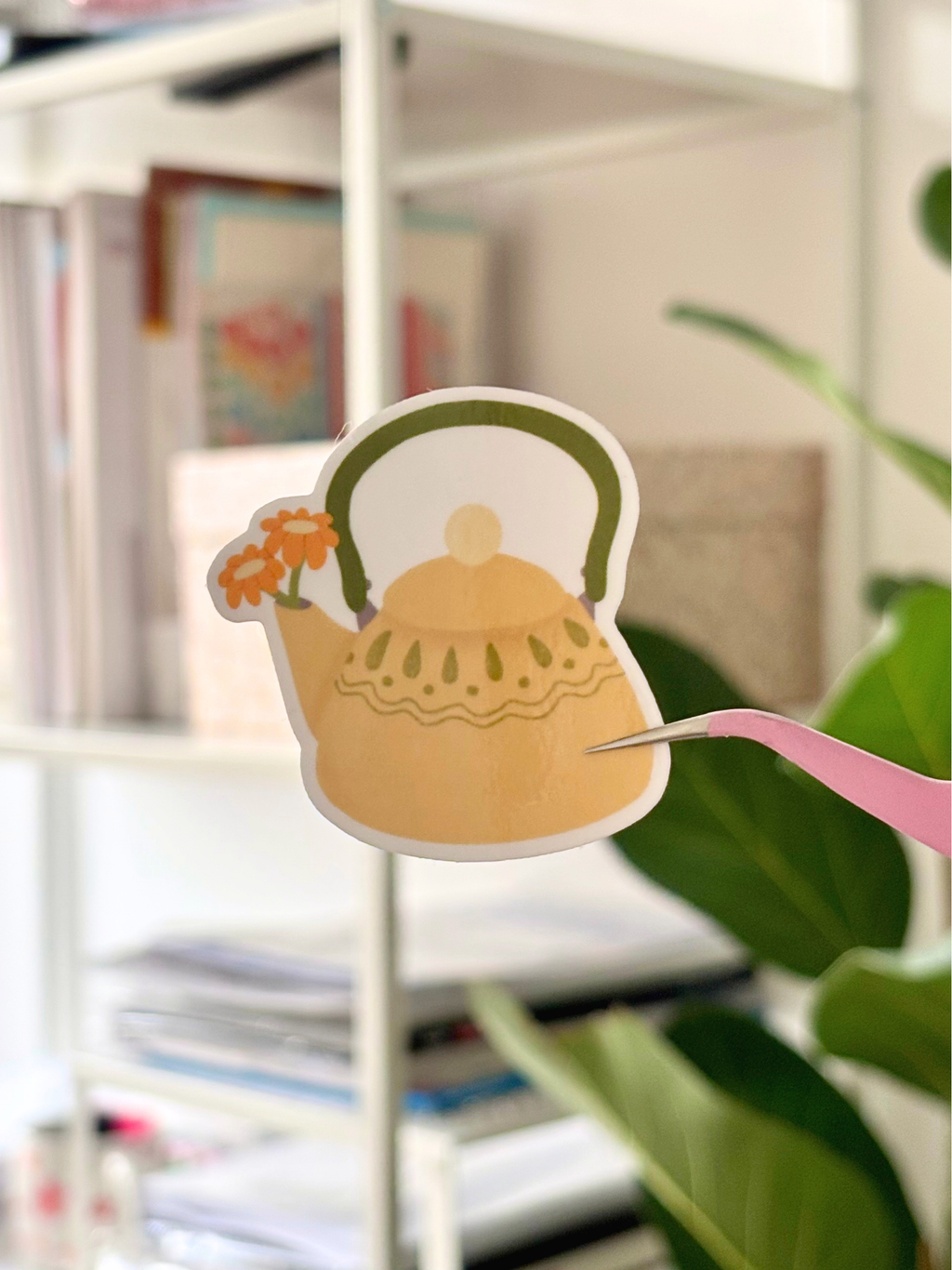Le sticker Théière fleurie tenu à la pince, pour donner l'échelle